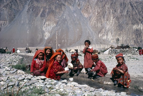 AFGHANISTAN, Tribal People, Kirghiz woman and children laughing as they wash pots in fresh water mountain stream.