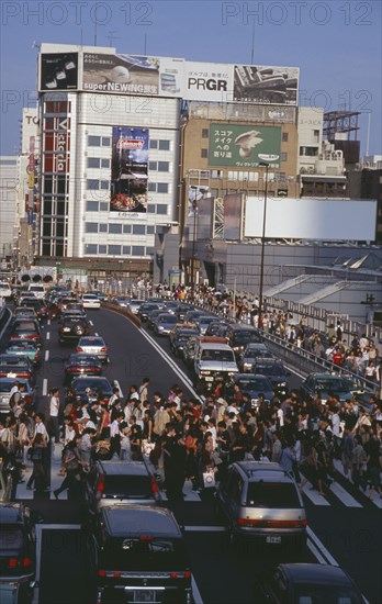 JAPAN, Honshu, Tokyo, Shinjuku. Crowded pedestrian crossing on busy city road with queues of traffic waiting to proceed