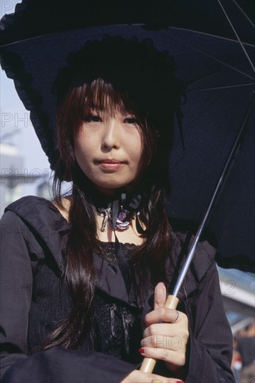 JAPAN, Honshu, Tokyo, Harajuku District. Portrait of a teenage girl dressed in black with a black parasol