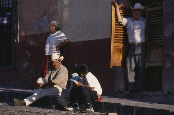 MEXICO, Guanajuato, San Miguel de Allende, Street scene with man and young boys in conversation sitting on pavement and man and woman standing behind.