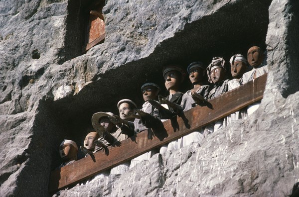 INDONESIA, Sulawesi, Toraja wooden funeral effigies or tau tau in cliff graves.  The figures accompany the dead from funeral house to burial ground and watch over both the living and dead.