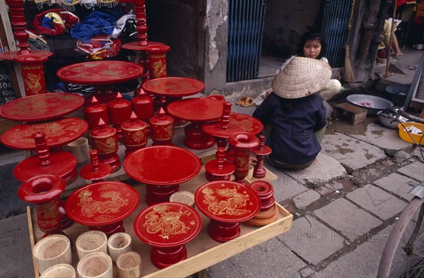 VIETNAM, North, Hanoi, Red lacquered dishes and pots displayed on pavement  with two women sitting at side.
