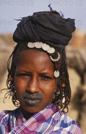 MALI, Tribal People, Head and shoulders portrait of Fulani woman with tattooed lips and wearing French coins in her hair.