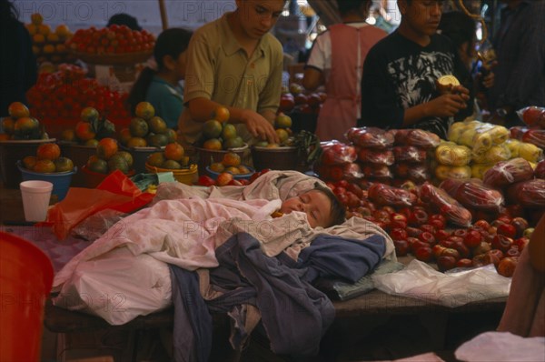 MEXICO, Oaxaca, Sleeping child on market stall selling fruit.
