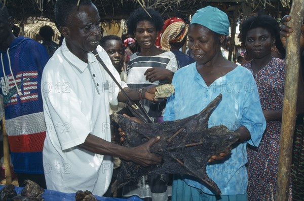GHANA, West, Markets, "Man purchasing dried grasscutter, a type of large rodent, from woman on market stall."