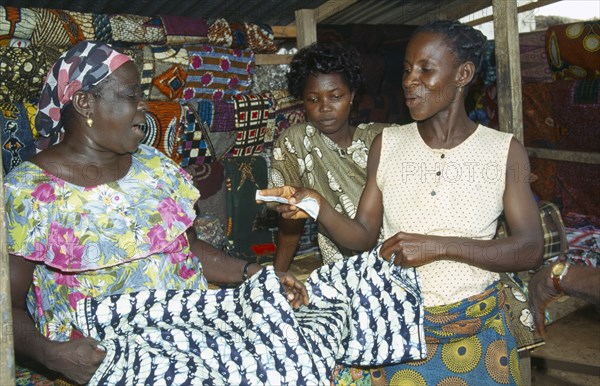 GHANA, West, Markets, Woman purchasing length of batik dyed cloth with fish design from market vendor.