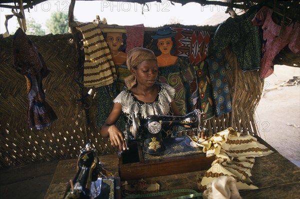 GHANA, Cheroponi, Dressmaker using an old Singer sewing machine in her workshop surrounded by fabrics