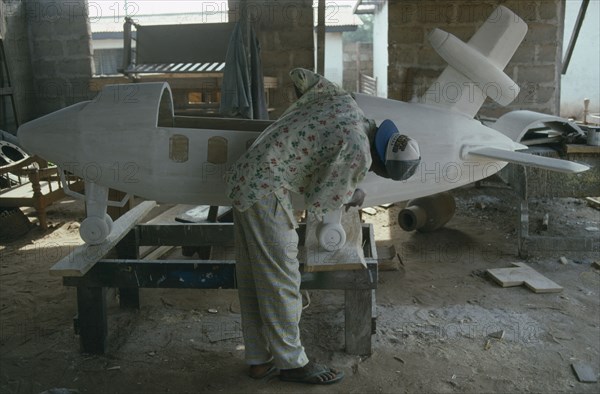 GHANA, Teshie, Kane Kwei brothers workshop.  Man painting and gluing together the wooden sections of a coffin in the form of an aeroplane for aircraft employee.