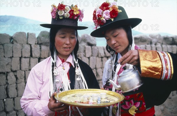 CHINA, Qinghai Province, Huzhu County, Women of Tu nationality and Lamaist Buddhist Yellow Hat sect preparing traditional welcome of three small glasses of alcoholic drink.