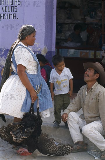 MEXICO, Oaxaca State, Tlacolula, Market day.  Woman holding turkey talking to man in street with small boy.