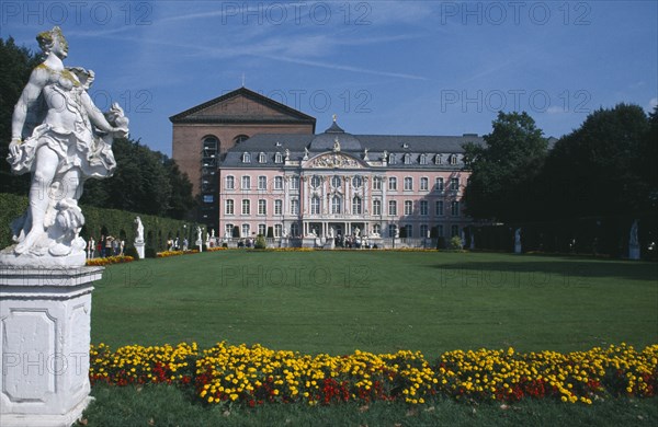 GERMANY, Rheinland Pfalz, Trier, Episcopal Palace.  Exterior facade and visitors with statue and flower bed in the foreground.
