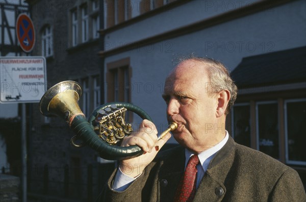 GERMANY, Rheinland Pfalz, Bernkastel, Man blowing hunting horn in town in the Mosel Valley.