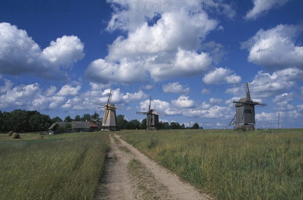 ESTONIA, Saaremaa Island, Dirt track leading to windmills in agricultural landscape with dramatic cloudscape above.