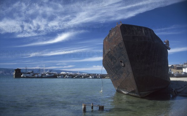 RUSSIA, Siberia, Lake Baikal, Rusting hull of ship in shallow water at lake shore.