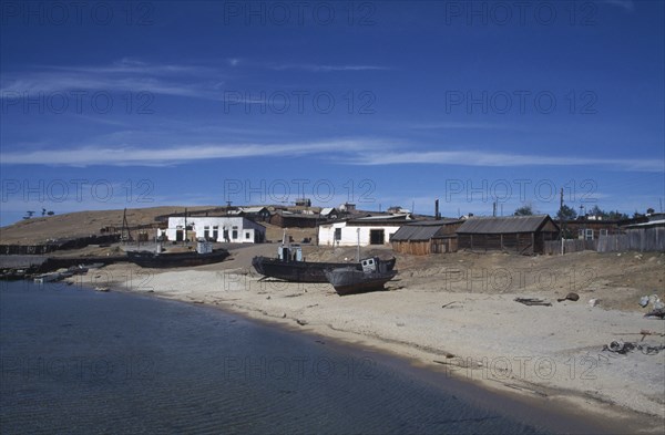 RUSSIA, Siberia, Lake Baikal, Fishing boats pulled up on lake shore with scattered buildings behind.