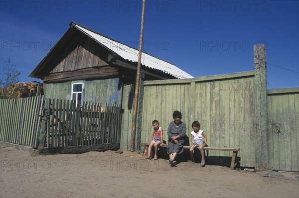 RUSSIA, Siberia, Lake Baikal, Buryat woman and children outside painted wooden fence of house.  The Buryat are of Mongolian descent and are the largest ethnic minority group in Siberia.