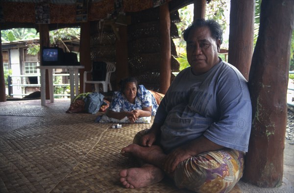 PACIFIC ISLANDS, Polynesia, Western Samoa, A Western Samoan tribal chief or Matai sitting on matting on floor inside house with television behind.
