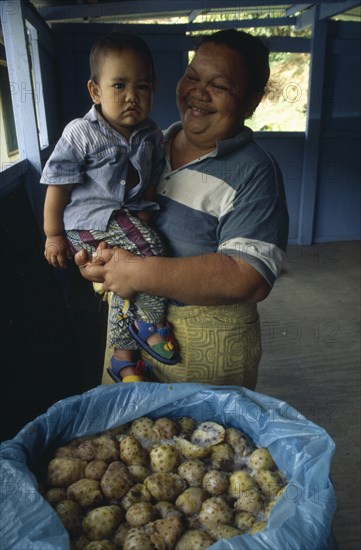 PACIFIC ISLANDS, Polynesia, French Polynesia, Marquesas Islands.  Taipivai Hiva.  Fermenting noni fruit with woman holding child behind.