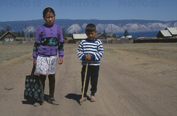 RUSSIA, Siberia, Lake Baikal, Buryat children with farmstead and lake behind.  The Buryat are of Mongolian descent and are the largest ethnic minority group in Siberia.