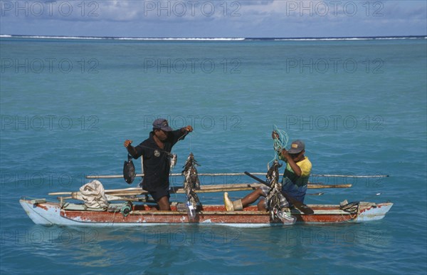 PACIFIC ISLANDS, Polynesia, Cook Islands, Aitutaki Lagoon.  Fishermen in wooden canoe pulling up fishing lines and catch.