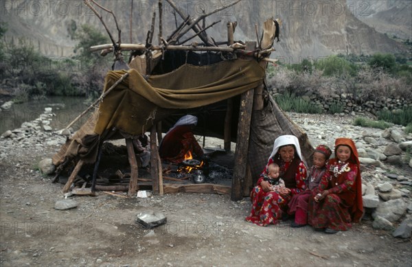 AFGHANISTAN, Tribal People, Kirghiz woman and children sitting outside tent while another woman cooks over wood fire inside.