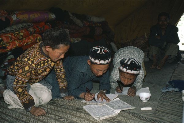 AFGHANISTAN, Tribal People, Kirghiz children writing inside yurt with man sitting beside doorway behind.