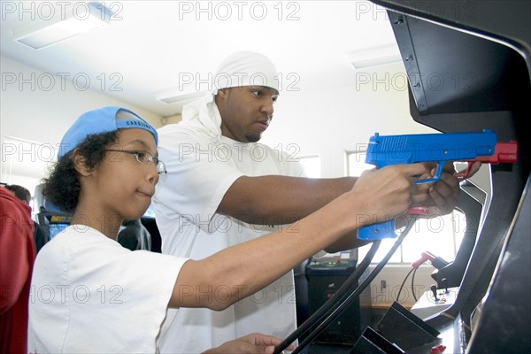 USA, Minnesota, St Paul, Youth Express Leader and member age 19 and 13 shooting Point Blank video game with red and blue replica 45 caliber plastic pistols.