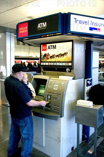 USA, Minnesota, Minneapolis, Father with baby son withdrawing cash at the ATM machine in the Minneapolis-St. Paul International Airport Charles Lindbergh Terminal.
