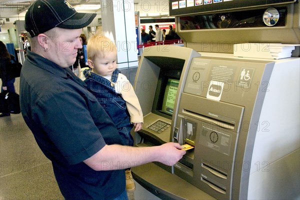 USA, Minnesota, Minneapolis, Father with baby son withdrawing cash at the ATM machine in the Minneapolis-St. Paul International Airport Charles Lindbergh Terminal.