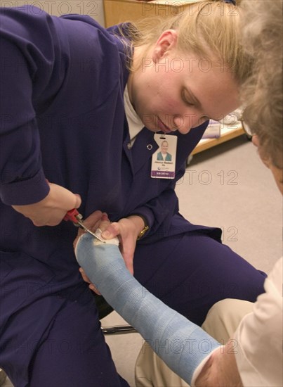 USA, Minnesota, Plymouth, Clinic nurse making adjustments to cast with cutter for elderly patient with a broken wrist