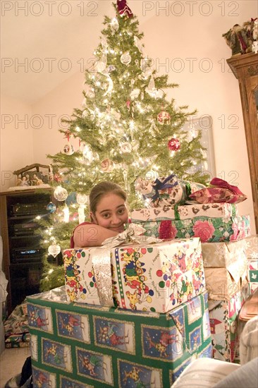USA, Minnesota, Brooklyn Center, Girl aged 12 happily surronded by piles of Christmas presents and decorated tree behind