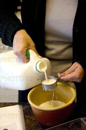 USA, Minnesota, St Paul, Woman age 30 measuring milk as an ingredient in a mixing bowl for waffles.