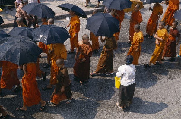 LAOS, Luang Prabang, Line of monks holding umbrellas to protect themselves with water being thrown during New Year celebrations.