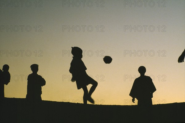 THAILAND, North, Children, Hilltribe kids playing football with a coconut silhouetted against evening sky.
