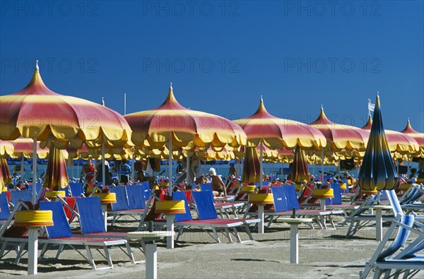 ITALY, Emilia-Romagna, Rimini, "Lines of red, yellow and blue parasols and sun loungers on sandy beach."