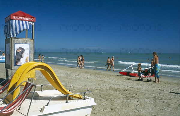 ITALY, Emilia-Romagna, Rimini, Adults and children on sandy beach with pedalo and lifeguard hut in foreground.