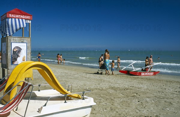 ITALY, Emilia-Romagna, Rimini, Adults and children on sandy beach with pedalo and lifeguard hut in foreground.