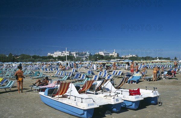 ITALY, Emilia-Romagna, Rimini, Busy beach scene with rows of striped sun loungers and pedalos in the foreground.