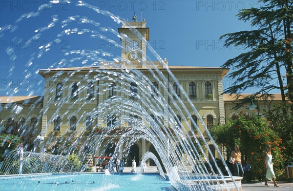 ITALY, Emilia-Romagna, Cattolica, Fountains in town square with building with clock tower behind.
