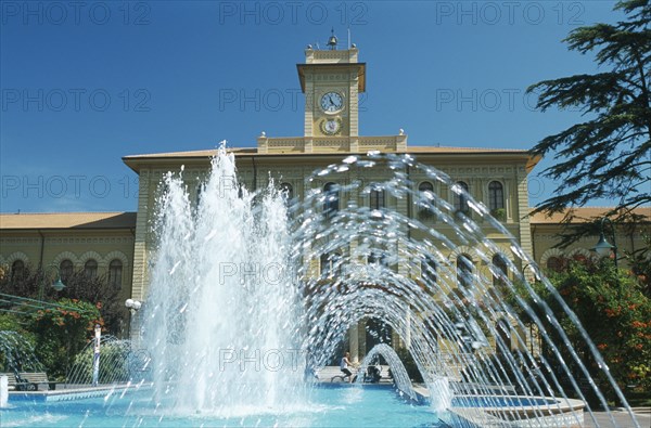 ITALY, Emilia-Romagna, Cattolica, Fountains in town square with building with clock tower behind.