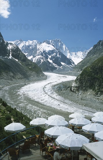 FRANCE, Rhone Alps, Haute Savoie, Chamonix.  People sitting at outside tables of terrace restaurant looking out across glacier and the Alps beyond.