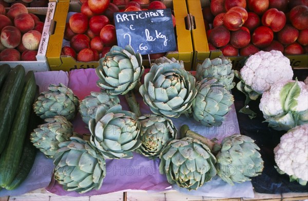 FRANCE, Rhone Alps, Haute Savoie, "Samoens.  Artichokes on market stall also selling cauliflower, cucumber and nectarines."