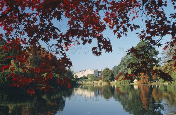 ENGLAND, East Sussex, Sheffield Park, Informal landscape garden initially laid out by Capability Brown in the 18th Century.  View across lake to house framed by trees in Autumn colours.