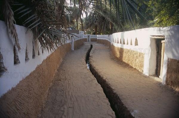 LIBYA, Ghadames, Deep irrigation channel through street between walls partly painted white with triangular cut outs.