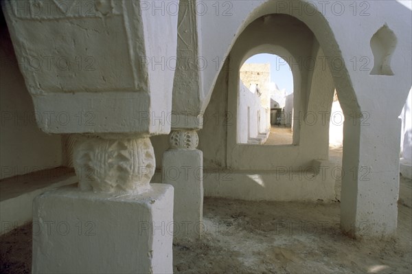 LIBYA, Ghadames, Tarasan Square.  Arched window in wall of passageway framing white painted town walls and man on bicycle.