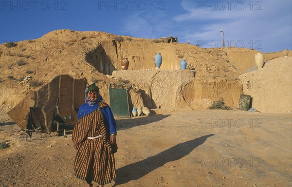TUNISIA, Zaraova, Portrait of a Berber woman standing outside her home which is dug out of a hillside