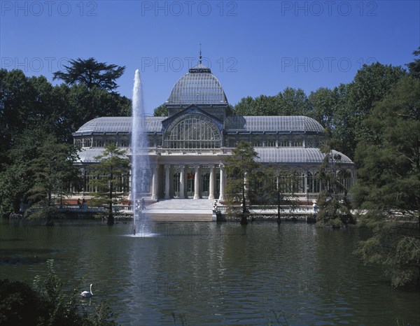 SPAIN, Madrid State, Madrid , Retiro Park. The Crystal Palace surrounded by trees seen from across pond with fountain.