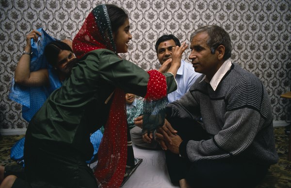 ENGLAND, Religion, Hindu, Daughter placing red mark on the forehead of her father during Hindu Sacred Thread Ceremony.