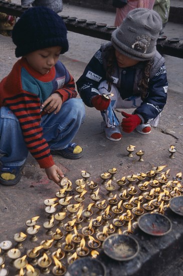 NEPAL, Patan, Children lighting oil wick candles at Kumbeshwar Mahadev Temple