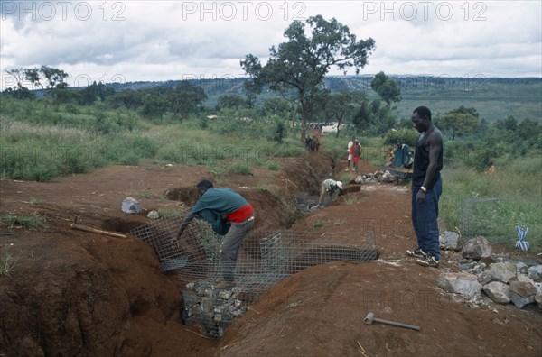 TANZANIA, West, Great Lakes Region, Refugees making gambions to prevent water erosion.  Base of structure is stone filled wire cages covered with earth.